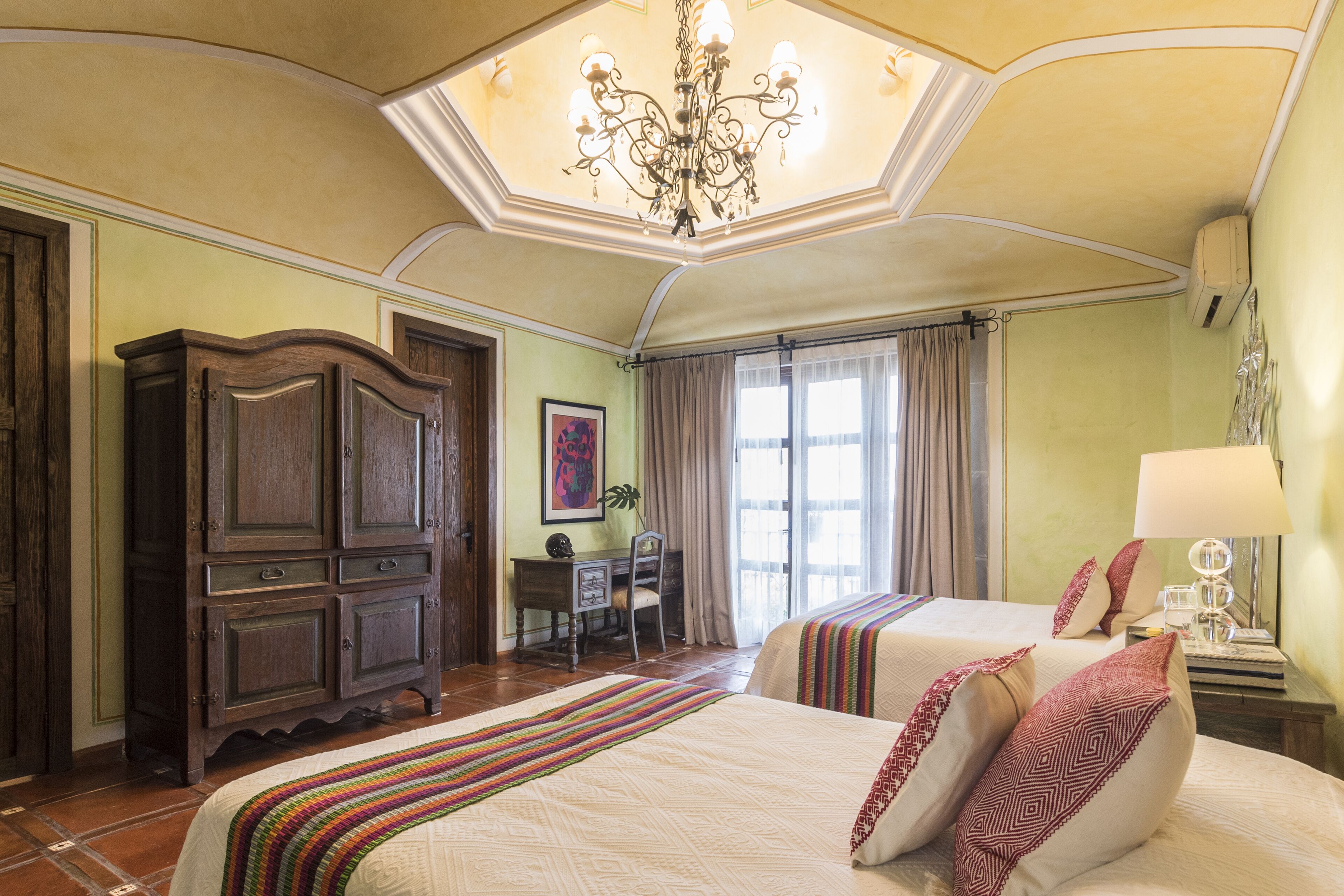 Ein Hotelzimmer mit zwei Betten, einem Schreibtisch, einem Sessel und einer Chandelier.