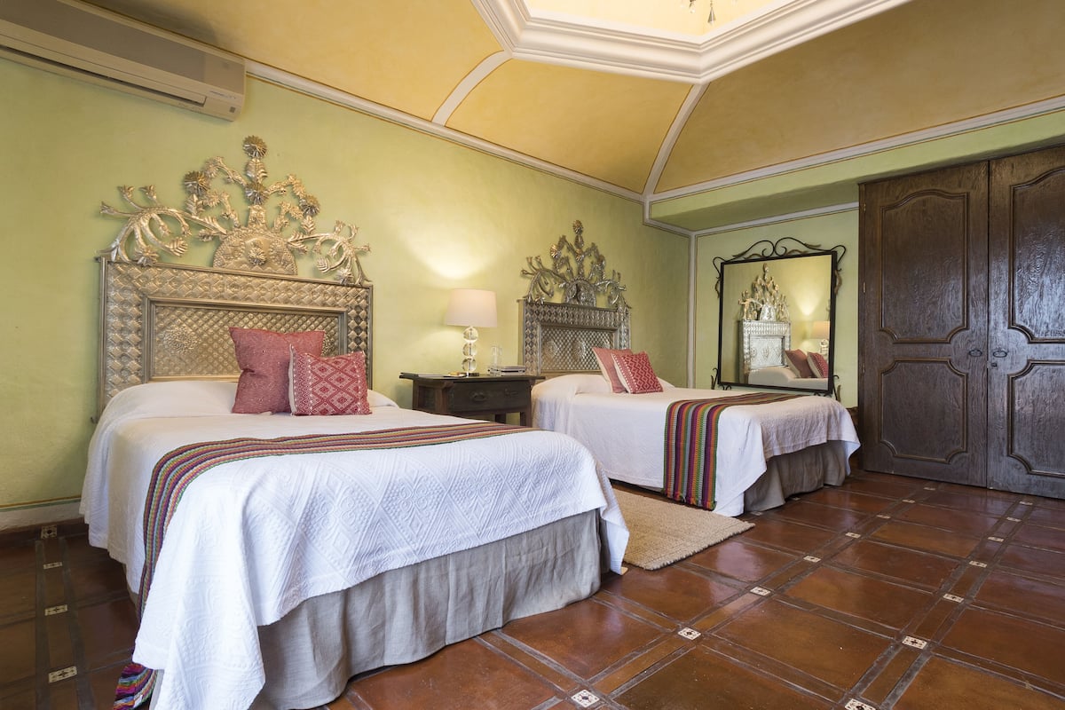 A hotel room with two beds, a large mirror, and a wooden wardrobe.