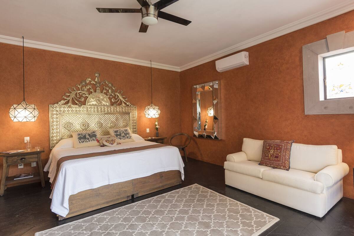 A bedroom with a bed, a sofa, a ceiling fan, and a large mirror.