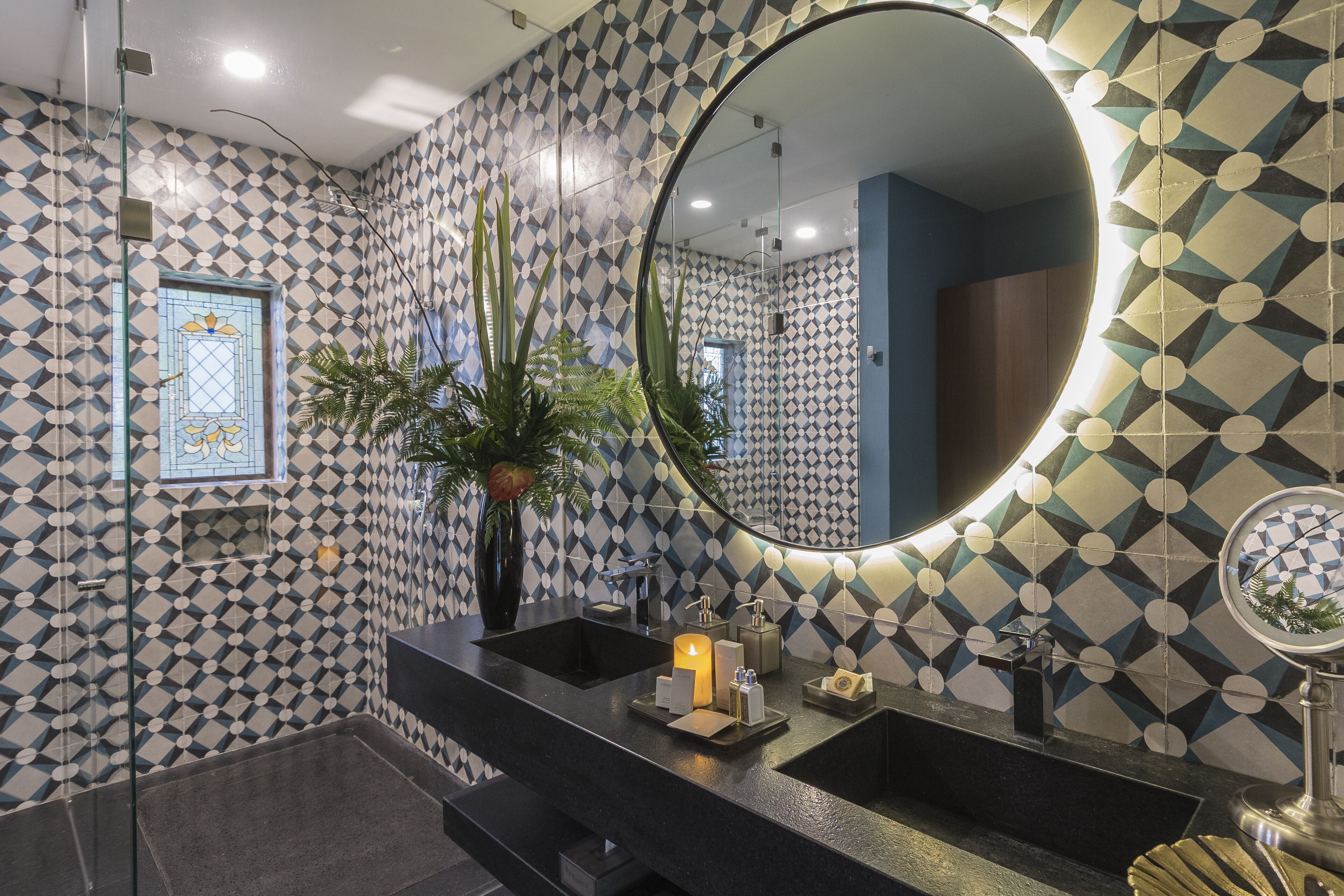 A bathroom with a geometric patterned wall, a large mirror, a black sink, and a potted plant.