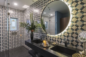 Un baño con pared de diseño geométrico, un espejo grande, un lavabo negro y una planta en maceta.