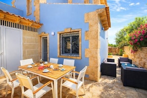A patio with a wooden table and chairs, a stone wall, and a window with metal bars.