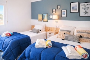 A hotel room with two beds, a nightstand, a lamp, and a wall with framed pictures.