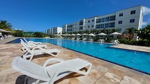 A swimming pool with white lounge chairs and umbrellas, surrounded by a multi-story building with balconies.