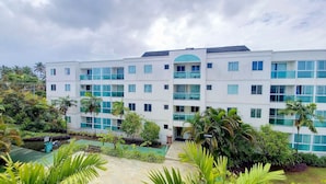 A multi-story hotel with a central courtyard, surrounded by lush greenery and palm trees. - Palm Village Acqua (Ipojuca)