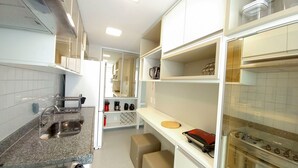 A compact kitchen with white cabinets, a granite countertop, a built-in oven, and a coffee machine. - Palm Village Acqua (Ipojuca)