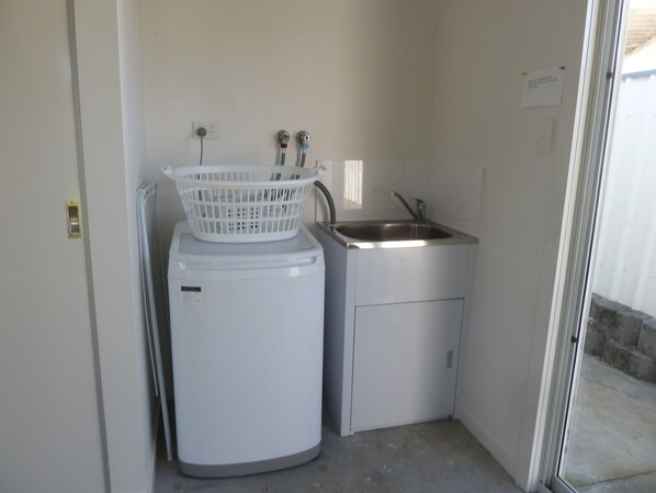 A compact laundry area with a washing machine, a sink, and a basket. - Close to shops, beaches, Bridport Distilling Co and eateries (Bridport)