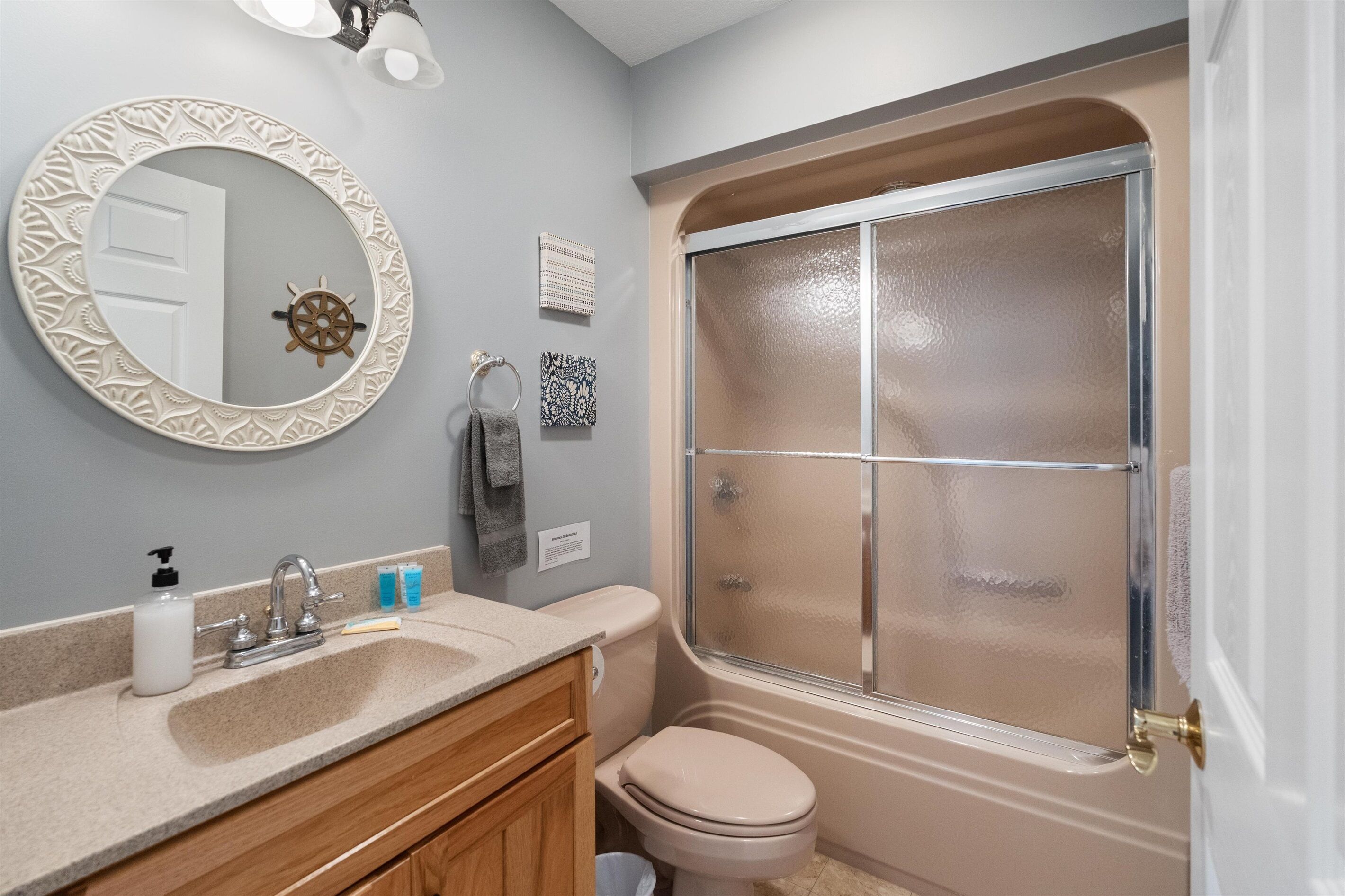 Une salle de bain avec un miroir rond, un lavabo doté d’un distributeur de savon, des toilettes et une douche à parois de verre.