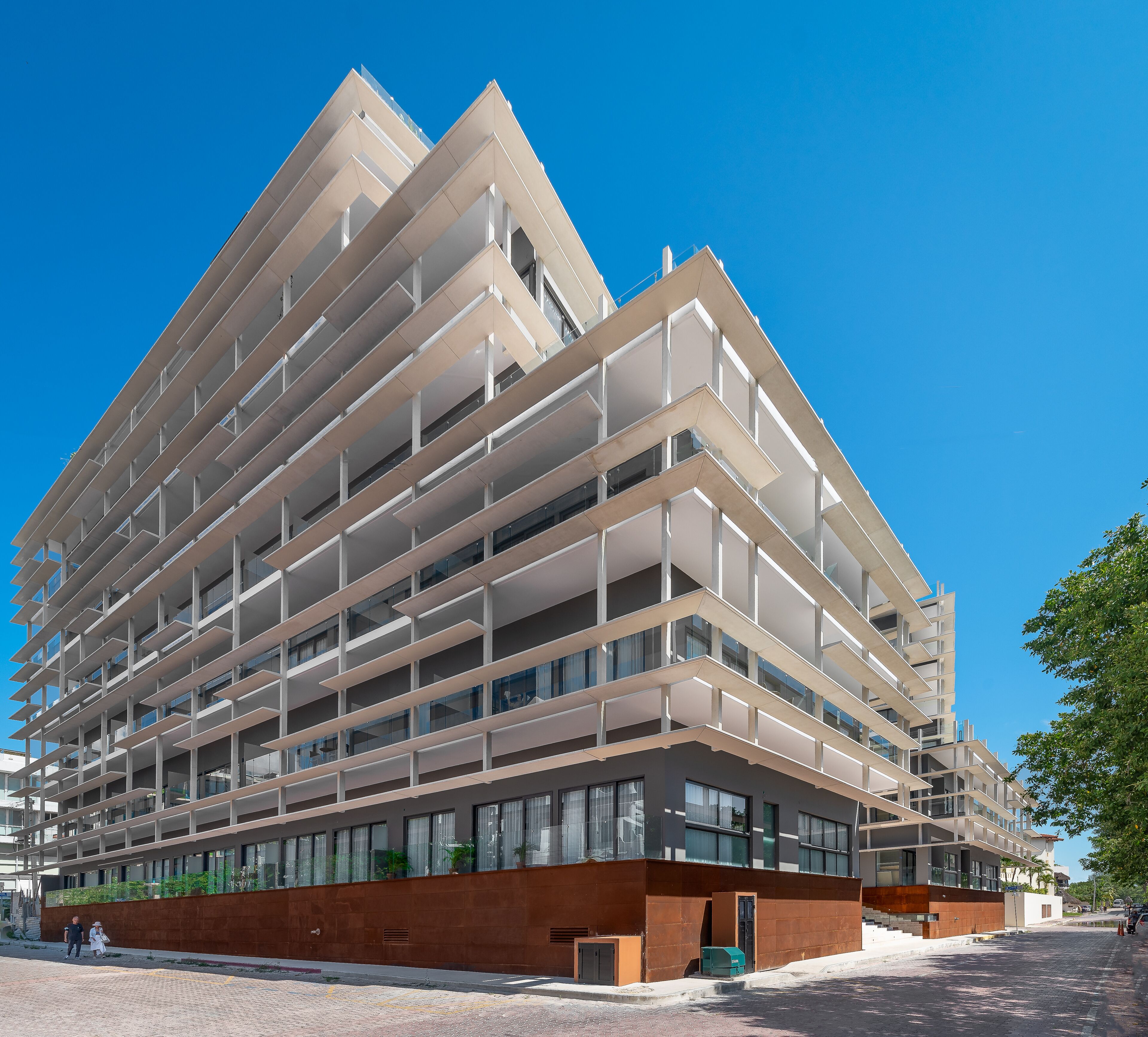 Um edifício moderno de vários andares com fachada geométrica marcante, grandes janelas e base em tijolo.