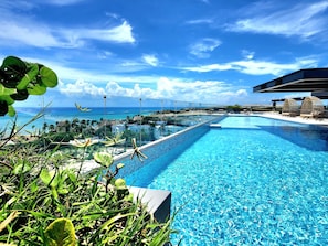 Une piscine d’un bleu éclatant, séparée du reste par une paroi de verre, entourée de plantes tropicales et offrant une vue imprenable sur la côte.