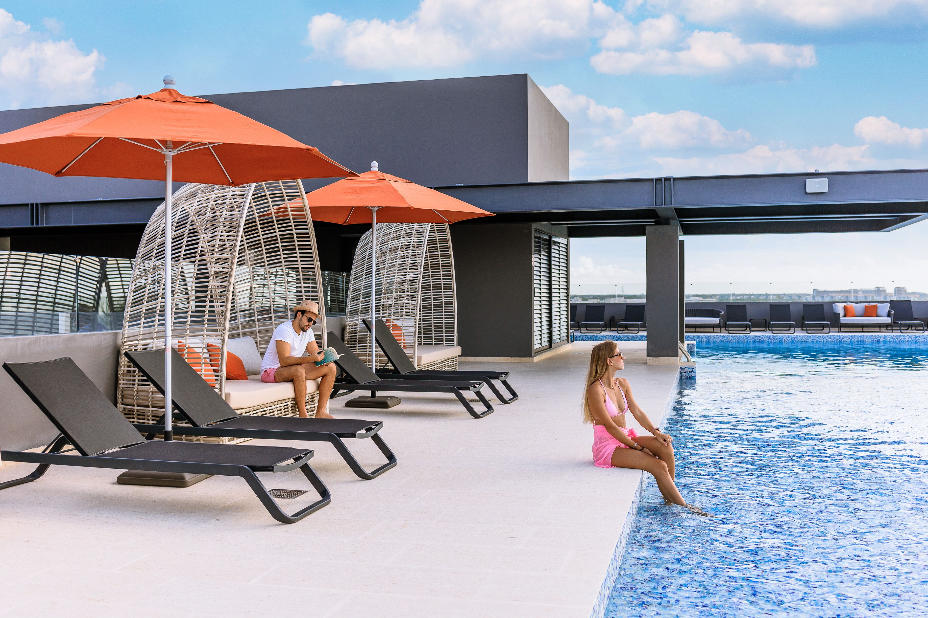 A poolside area with lounge chairs and umbrellas, a modern building in the background, and a clear sky.