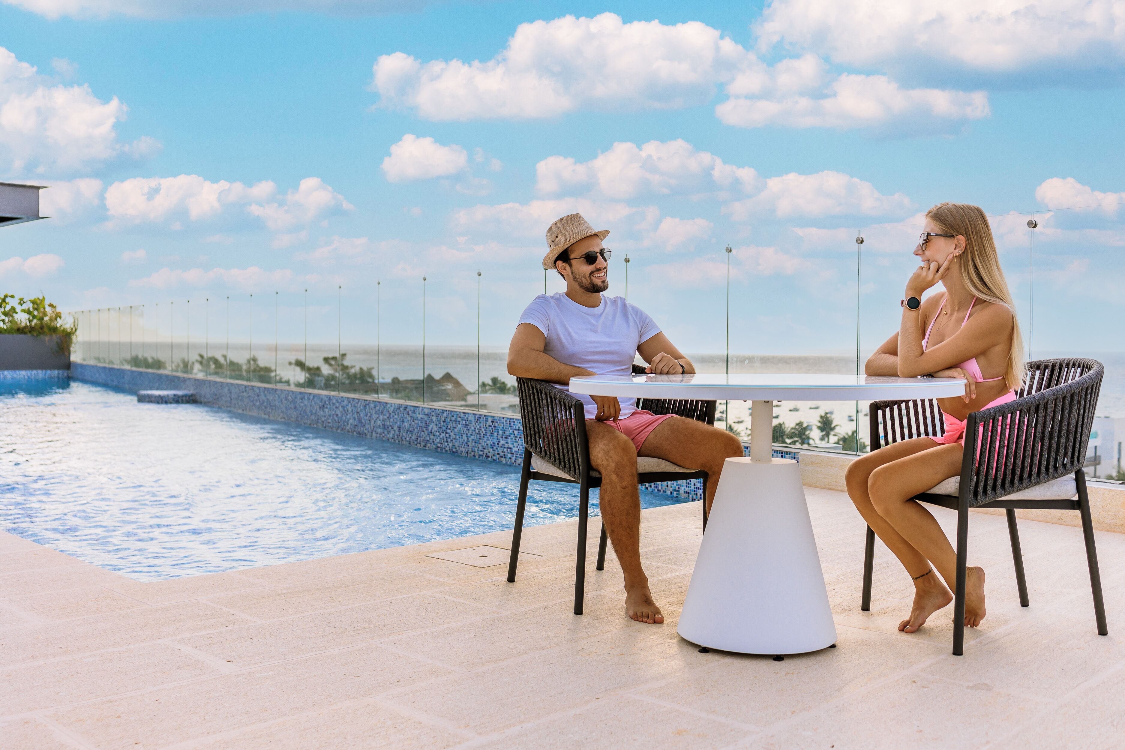 Two people seated at a table by a poolside with a clear view of the ocean in the background.