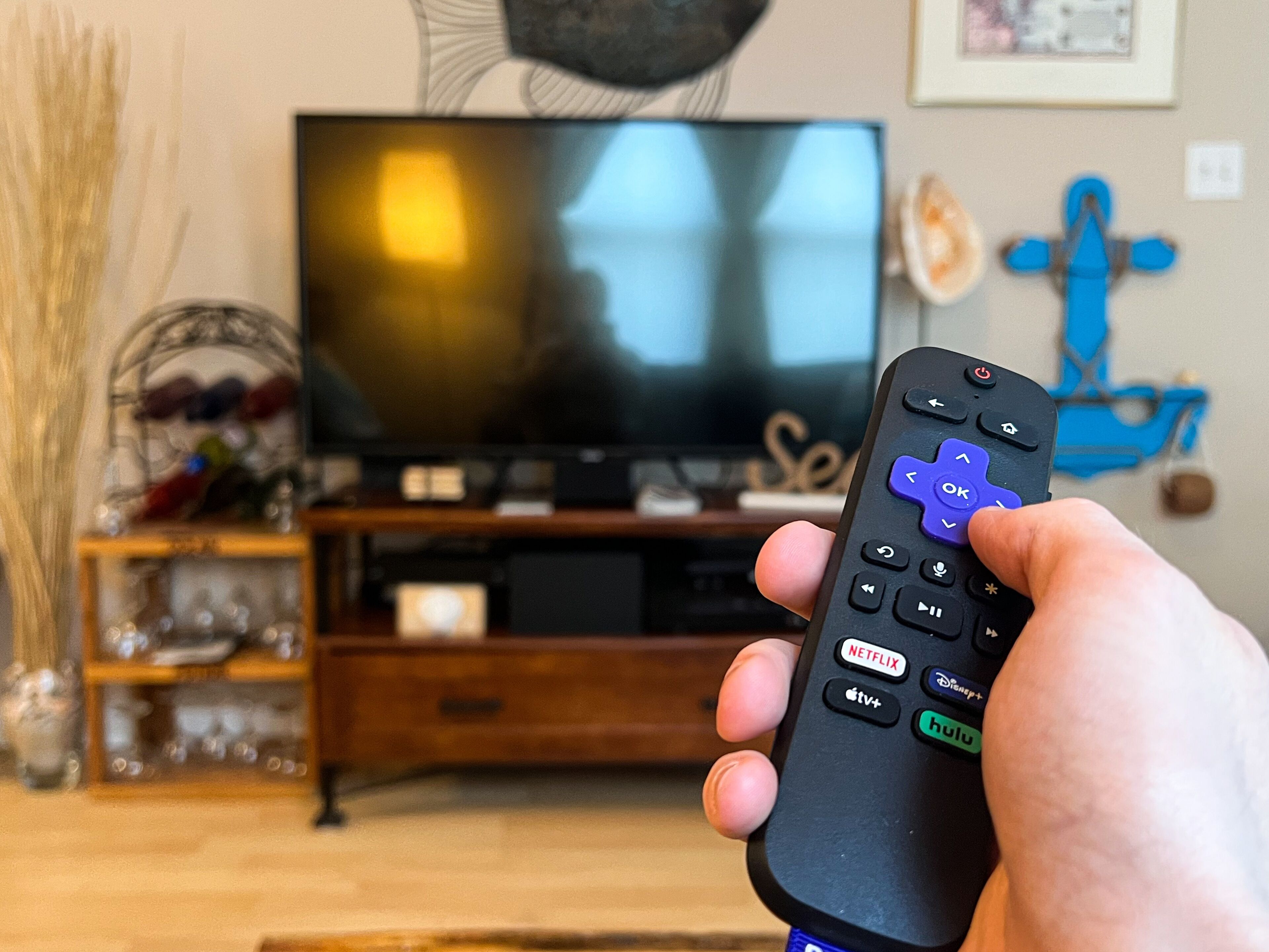 Une main tenant une télécommande, avec un téléviseur en arrière-plan.