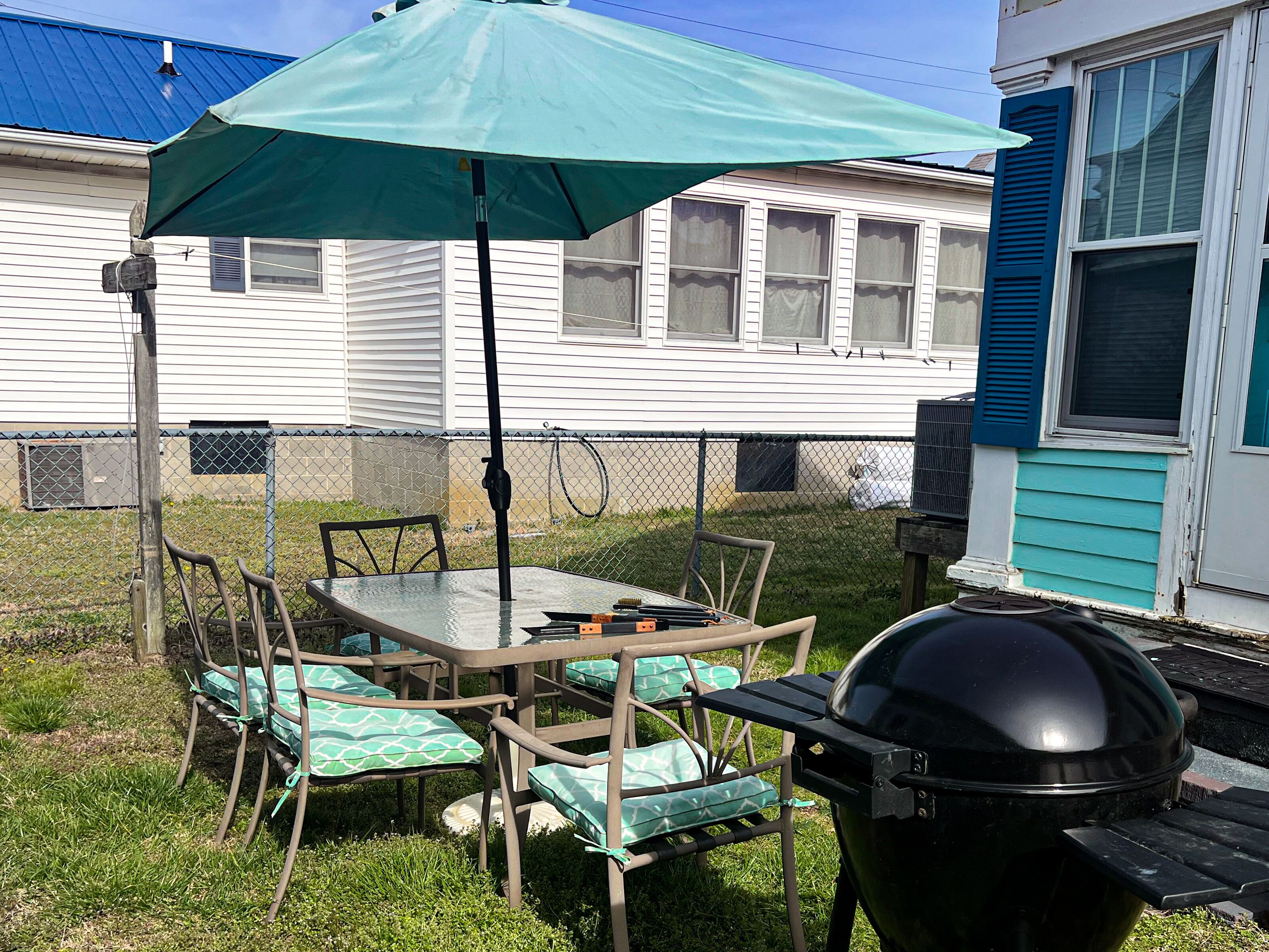 Un patio trasero con mesa y sillas, una parrilla y un área de patio techada.