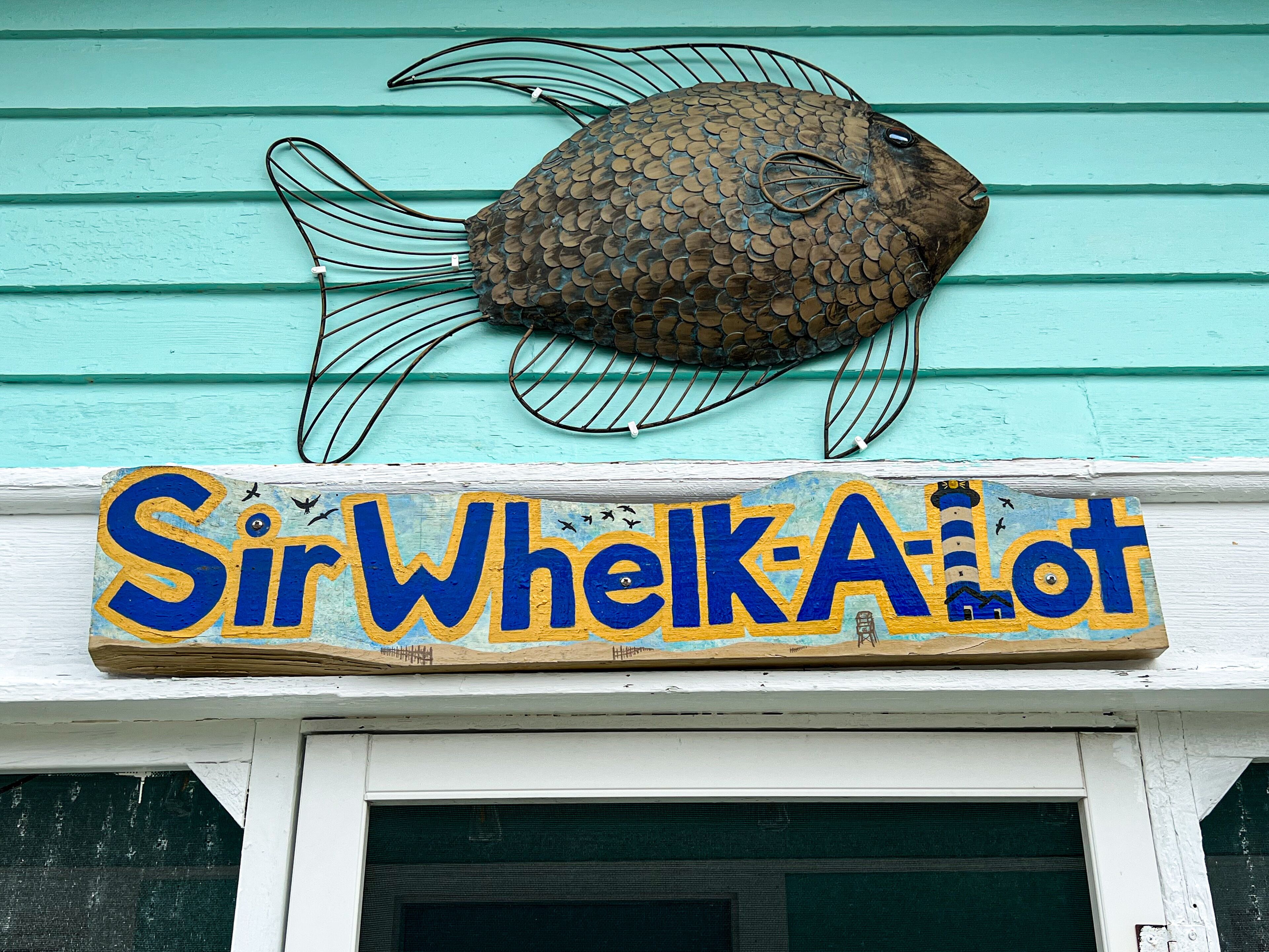 Un objet décoratif en forme de poisson et une enseigne sur laquelle on peut lire « SirWhelkA’lot ».