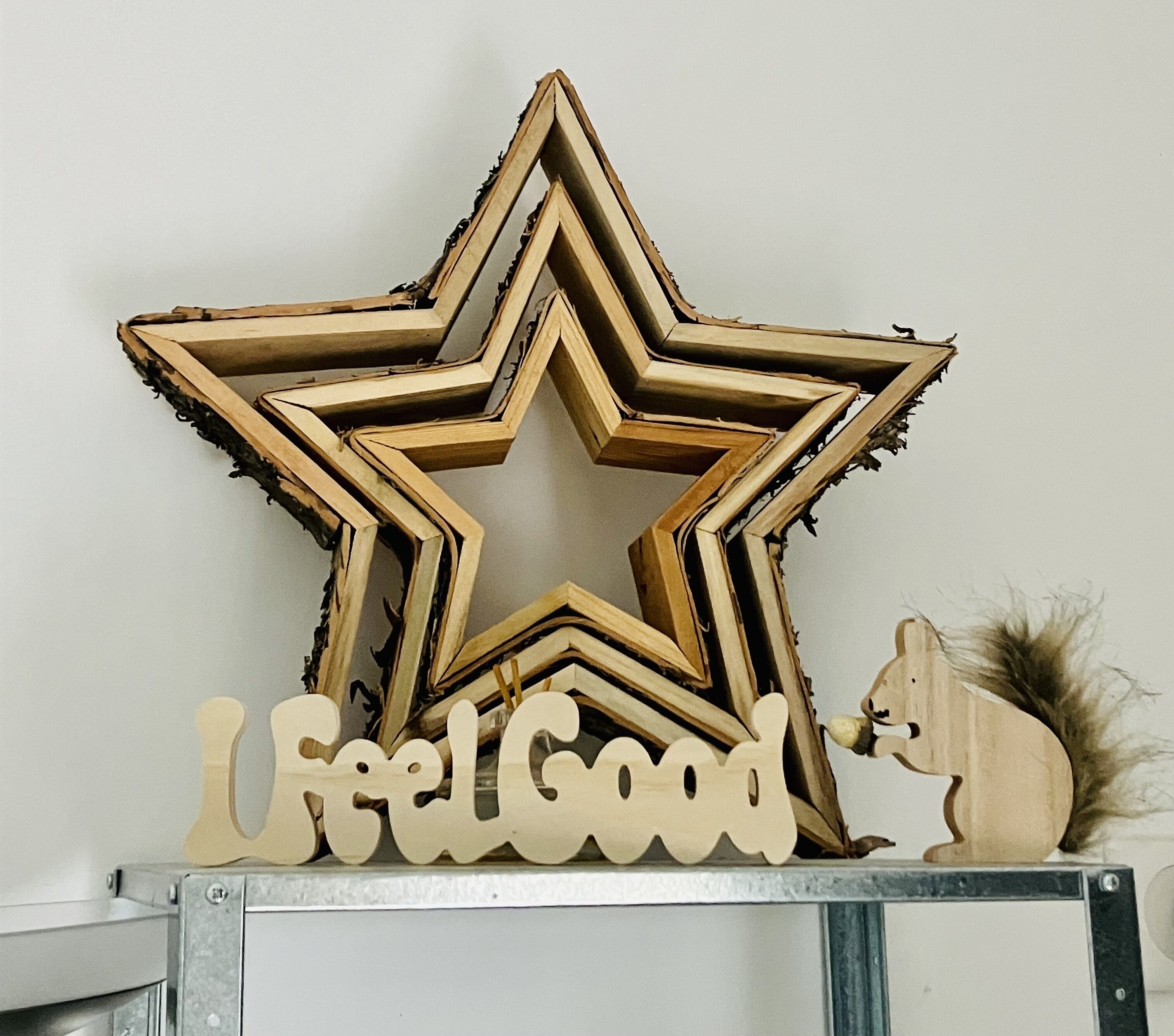 A wooden star decoration with the words "Feel Good" below it, placed on a shelf.