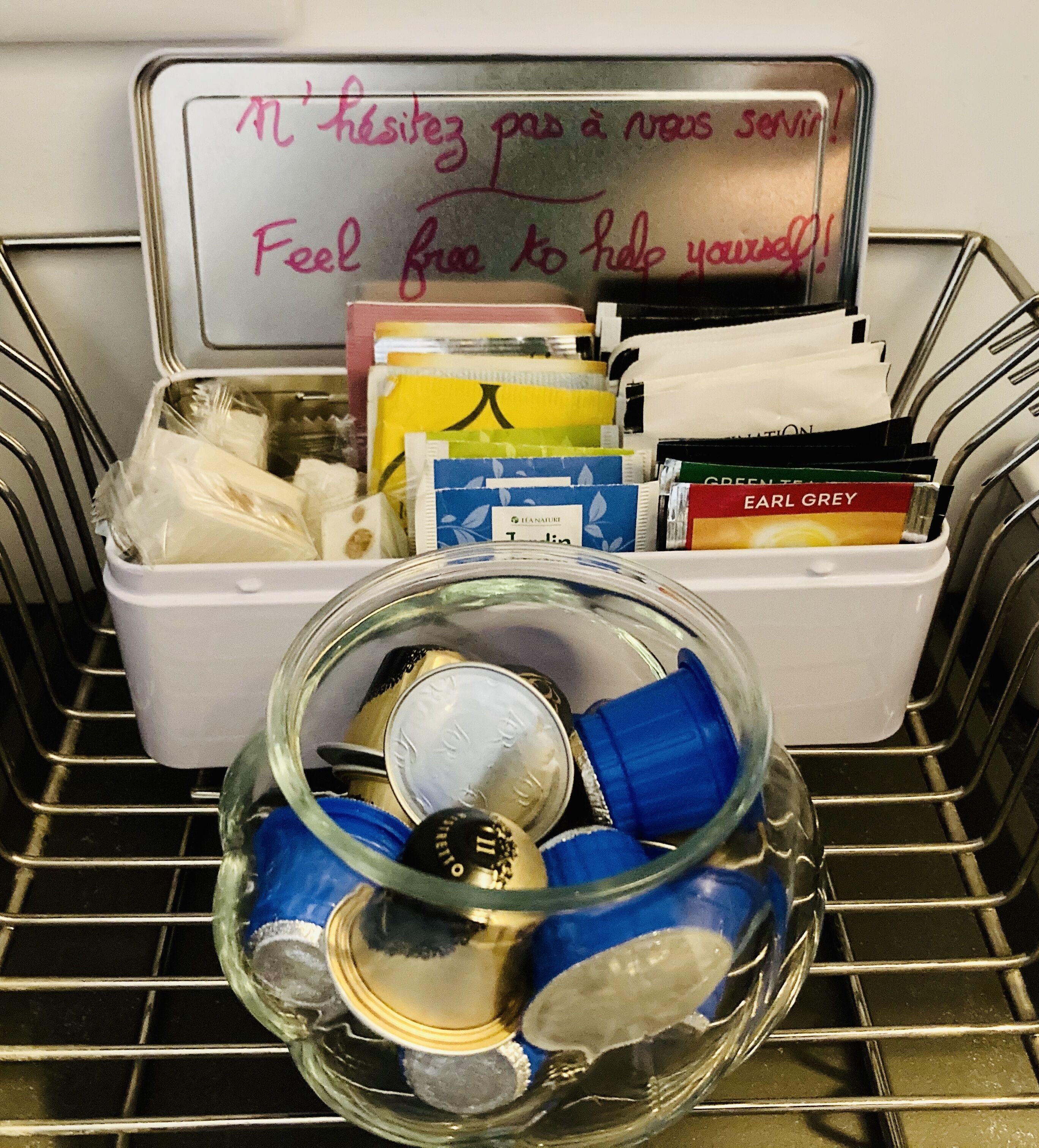 Een opbergkist met een handgeschreven briefje, gevuld met verschillende spullen zoals boeken en een glazen pot met blauwe deksels.