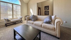 A living room with a high ceiling, a large arched window, a beige sofa, a small table, and a chair. - The Erie Home: Warm and Spacious in South Tulsa (Tulsa)