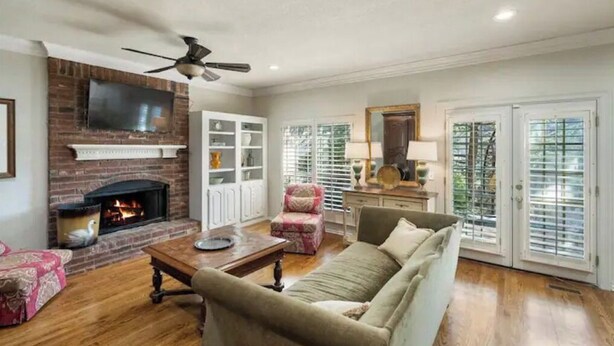 A living room with a fireplace, a ceiling fan, and a television mounted on the wall. - The Erie Home: Warm and Spacious in South Tulsa (Tulsa)