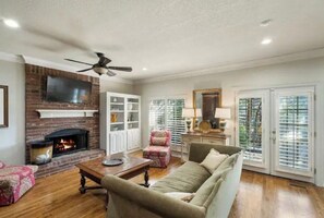 A living room with a fireplace, a ceiling fan, and a television mounted on the wall. - The Erie Home: Warm and Spacious in South Tulsa (Tulsa)