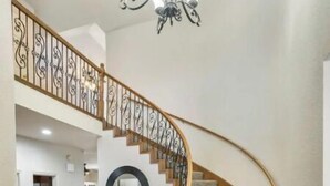 A curved wooden staircase with a metal railing, carpeted steps, and a chandelier. - The Erie Home: Warm and Spacious in South Tulsa (Tulsa)