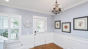A hallway with white paneled walls, a wooden floor, and a chandelier. - Kappi’s Luxury Coastal Retreat (North Charleston)