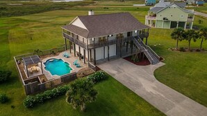 A two-story house with a swimming pool, a covered patio, and a staircase leading to a deck. - Secluded Getaway with Pool and Game Room (Galveston)