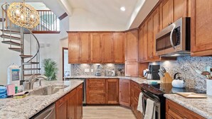A modern kitchen with wooden cabinets, granite countertops, a built-in oven, and a stainless steel microwave. - Secluded Getaway with Pool and Game Room (Galveston)