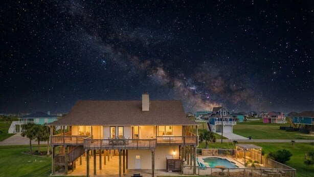 A two-story house with a balcony, a swimming pool, and a well-maintained lawn. - Secluded Getaway with Pool and Game Room (Galveston)