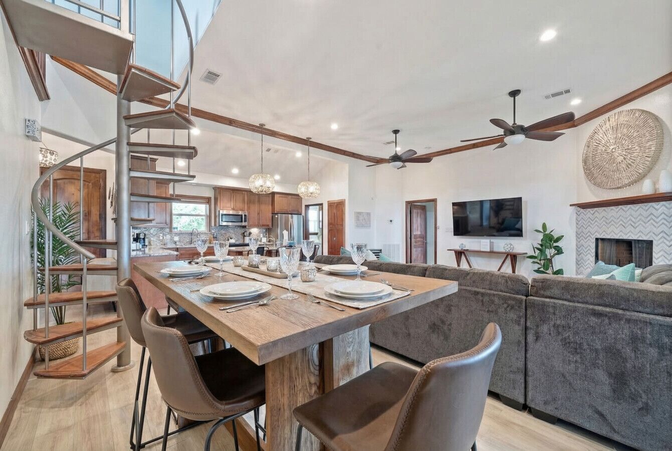 Una cocina amplia con una isla central, una escalera en espiral y un comedor con una mesa larga dispuesta para seis comensales.