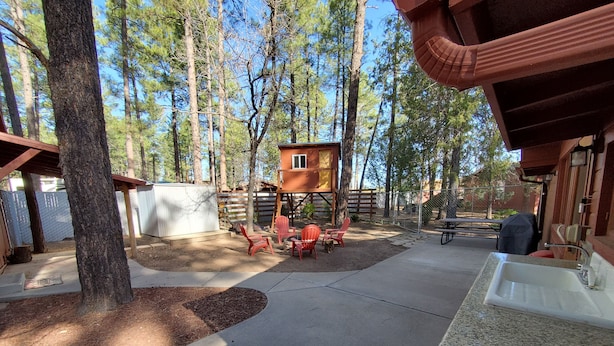 Un espacio al aire libre techado con una terraza de madera, sillas Adirondack rojas y una mesa de picnic.
