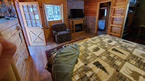 Una cabaña acogedora con interior de madera, chimenea, televisión y cama con colcha.