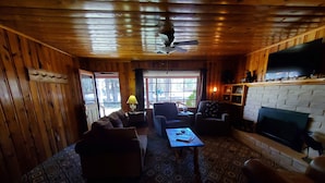 Interior acogedor de una cabaña con techo de madera, chimenea, televisor y piso con diseño.