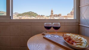 A table with two wine glasses and a plate of food by a window overlooking a cityscape.