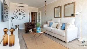 A modern living room with a white sofa, two large wall clocks, a round coffee table, and a hanging light fixture.