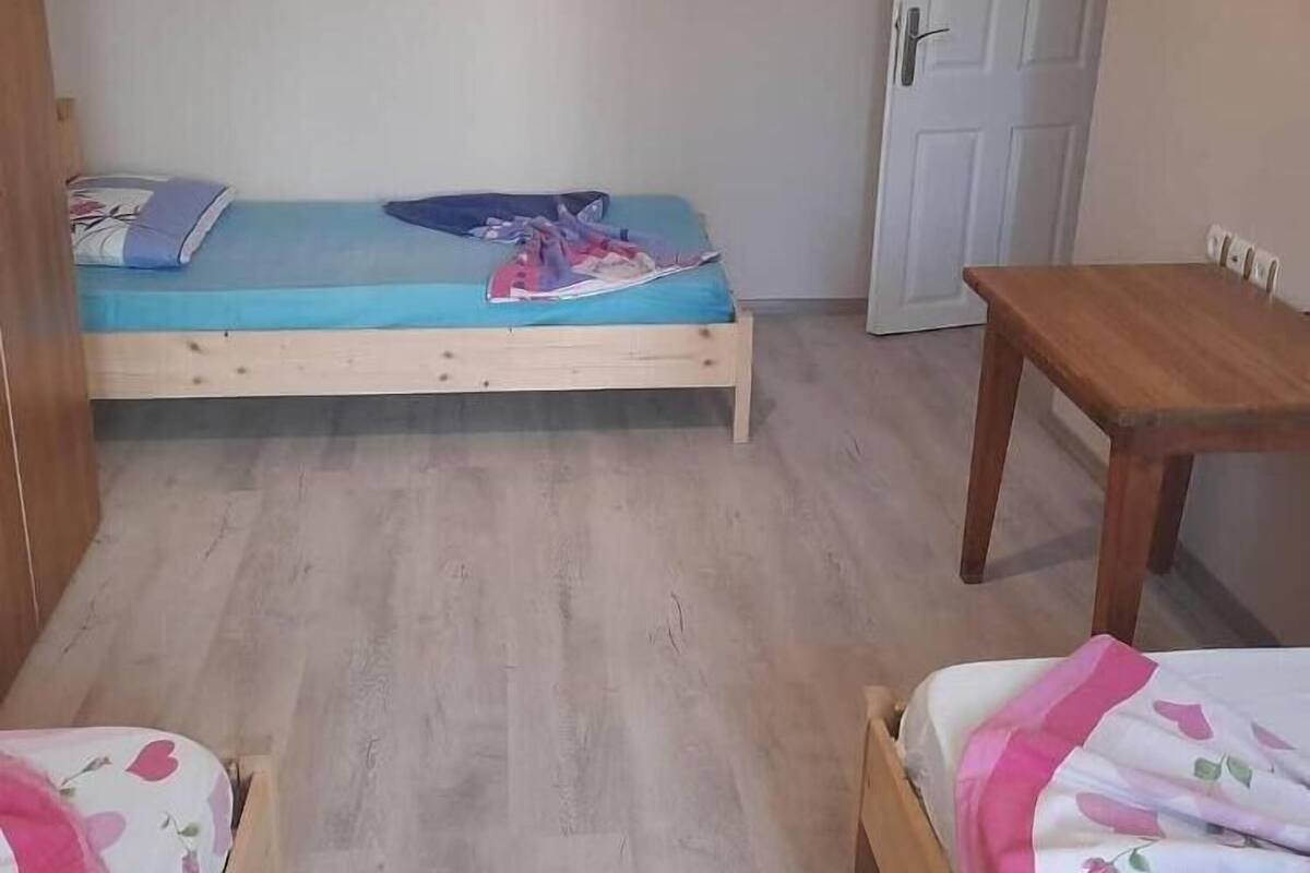 Quarto pequeno com uma cama de solteiro, uma mesa de madeira e uma porta.