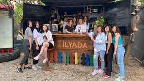 A group of people posing in front of a small outdoor kiosk with a wooden counter labeled "ILYADA". - İlyada Pansiyon (Cide)