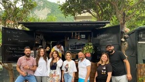 A group of people standing in front of a small outdoor café with a blackboard menu. - İlyada Pansiyon (Cide)