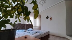 A bedroom with a bed, a potted plant, and a table with slippers. - İlyada Pansiyon (Cide)