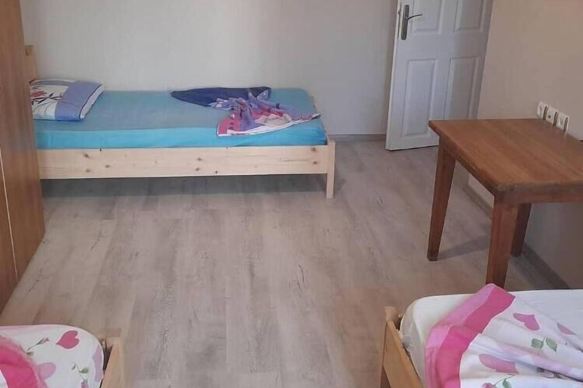 Acomodação pequena, com um quarto, uma cama de madeira, uma mesinha e um guarda-roupa.