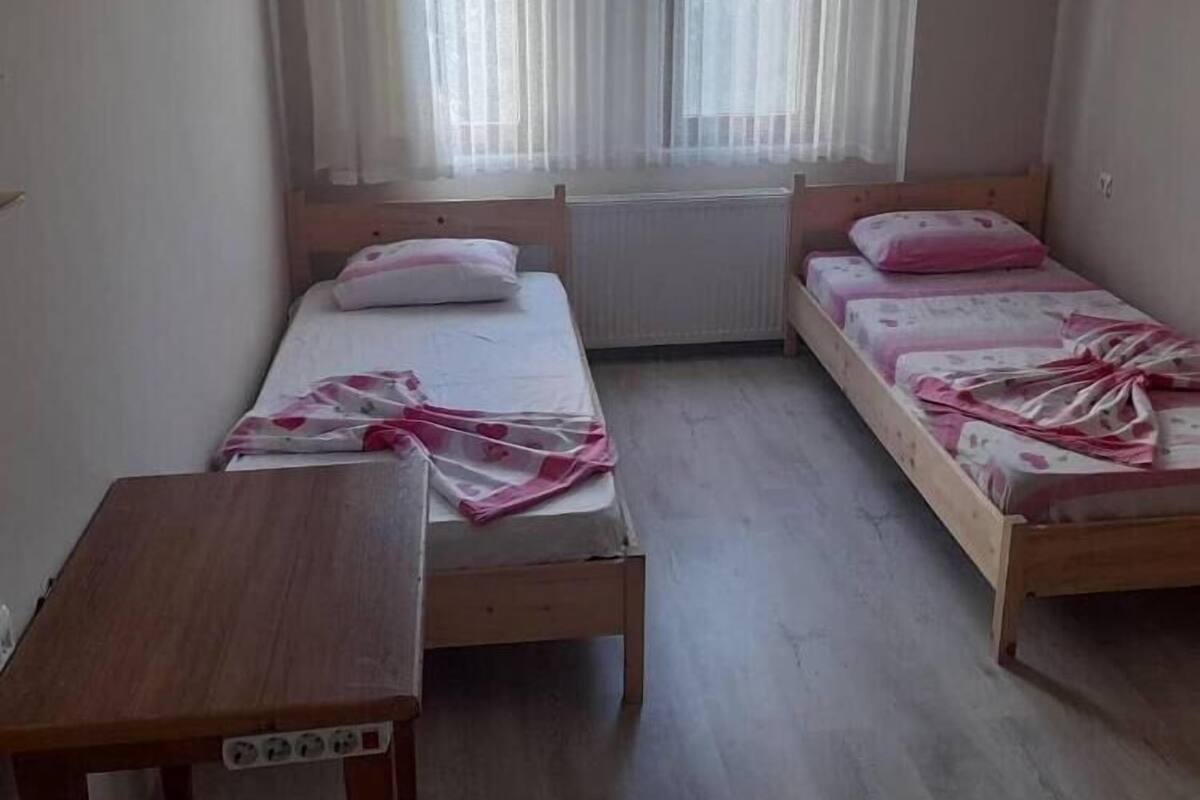 Quarto pequeno e limpo com duas camas de solteiro, uma mesa de madeira e um radiador.