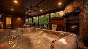 A hot tub in a rustic cabin with a stone fireplace and wooden beams.