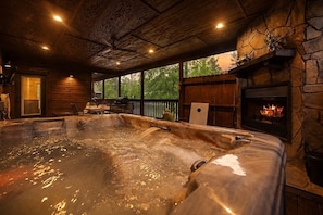 A hot tub in a rustic cabin with a stone fireplace and wooden beams.