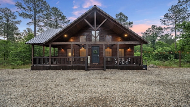 A log cabin with a porch, a welcome sign, and a gravel driveway.