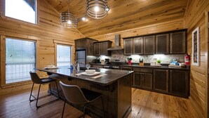 A modern kitchen with wooden walls, a central island, bar stools, and a large window.