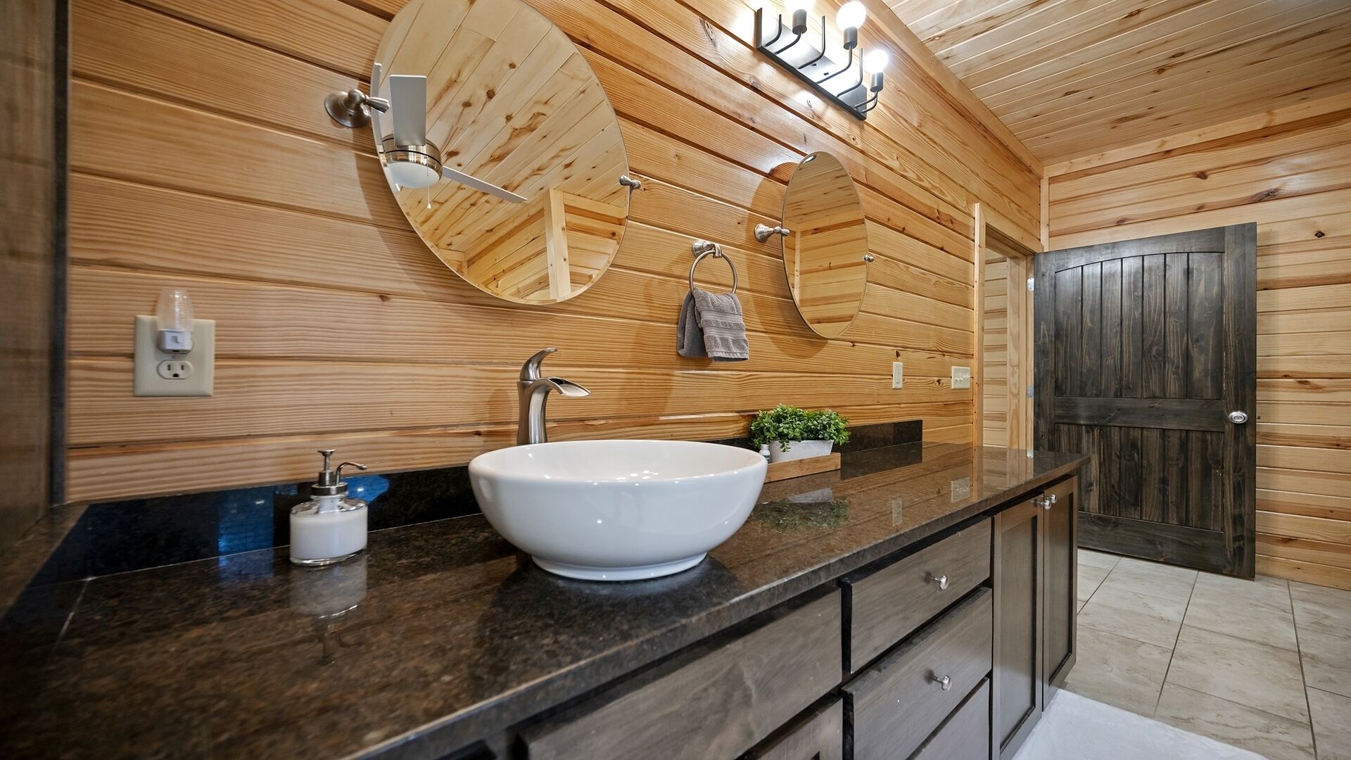 A modern bathroom with a large oval sink, wooden panel walls, a mirror, a towel rack, and a door.