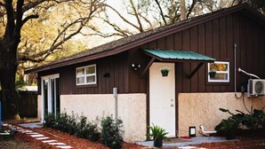A single-story building with a brown exterior and a green roof, a small porch with potted plants, and a pathway leading to the entrance. - 5 springs 4 to 10 minutes away Goats, Chickens, Free Eggs, Memories FARM Setting (Apopka)