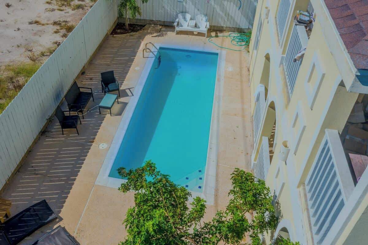 A rectangular swimming pool with a deck, surrounded by a low wall and a building with arched windows.