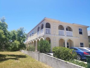 A two-story building with a light beige facade, multiple balconies, and a concrete retaining wall. - Clean Pool Walk to Beach - Pet Ok - Ground Floor (South Padre Island)