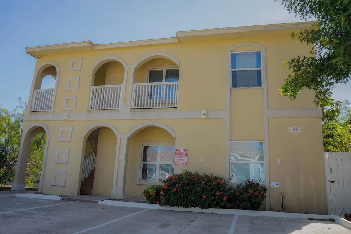 A two-story building with a yellow facade, multiple balconies, and a gated entrance.